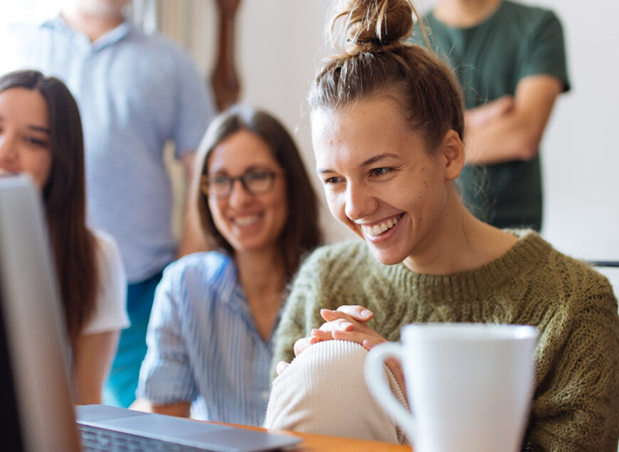 Smiling team collaborating around laptop with coffee