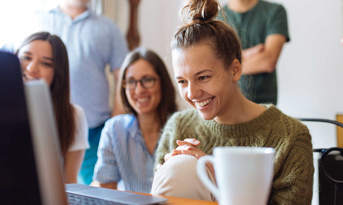 Smiling team collaborating around laptop with coffee