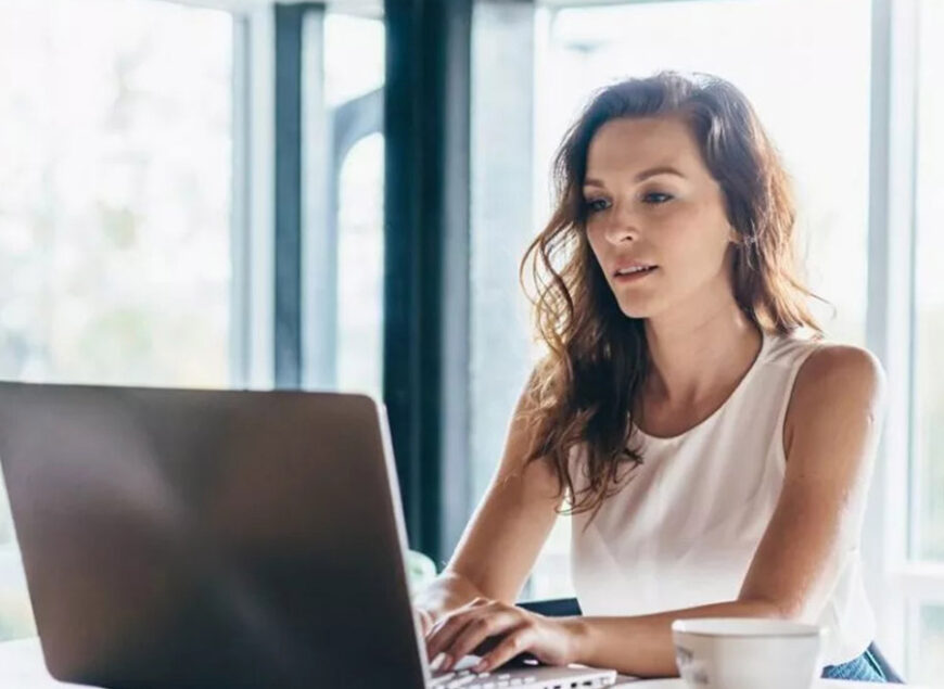Woman working on laptop by window with coffee