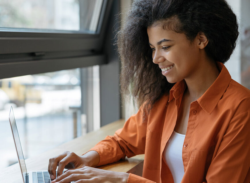 Smiling woman typing on laptop by window