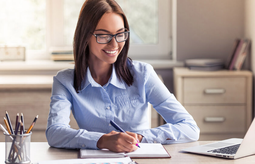 Smiling woman writing at desk with laptop