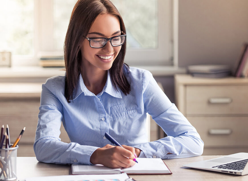 Smiling woman writing at desk with laptop