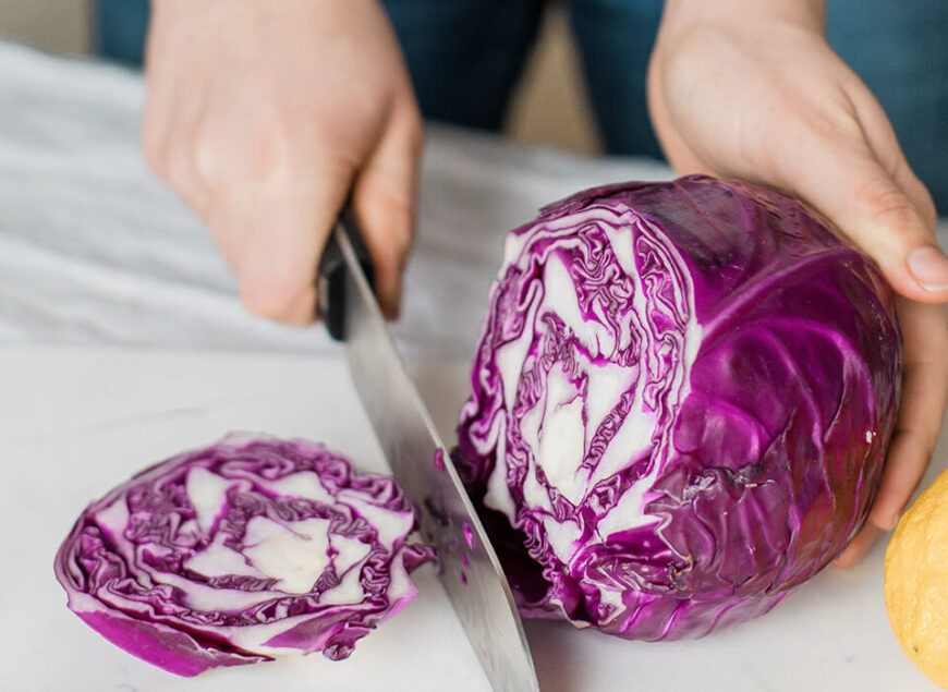 Hands slicing purple cabbage on cutting board