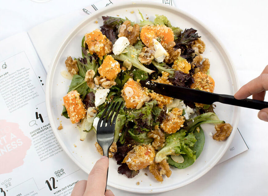 Person cutting roasted sweet potato and greens salad