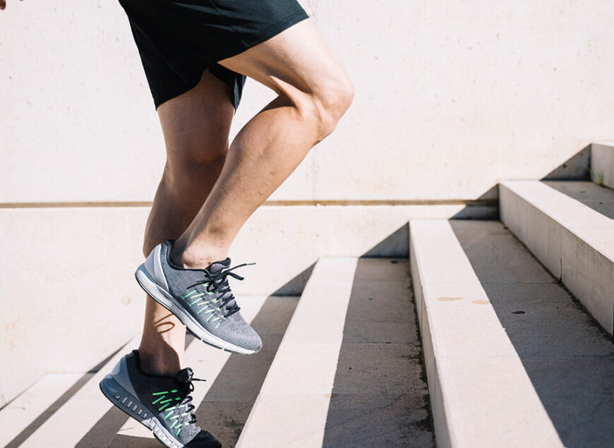 Runner's legs climbing sunlit concrete stairs